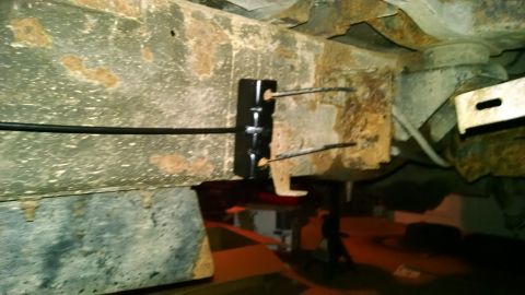 1994 Ford Bronco - A close-up view of the underside of a vehicle frame, showing rusted metal and a black bracket with two wires or cables attached. The vehicl…