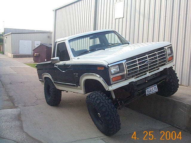 Lifted 1980s Ford Bronco with two-tone paint, angled on a concrete ledge.