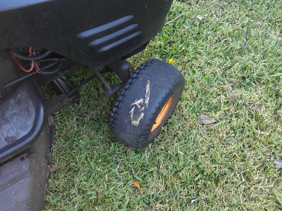 Black riding lawn mower rear tire and fender on grass.