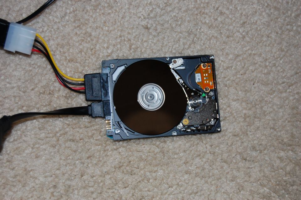 Disassembled hard drive with SATA cables connected, lying on carpet.