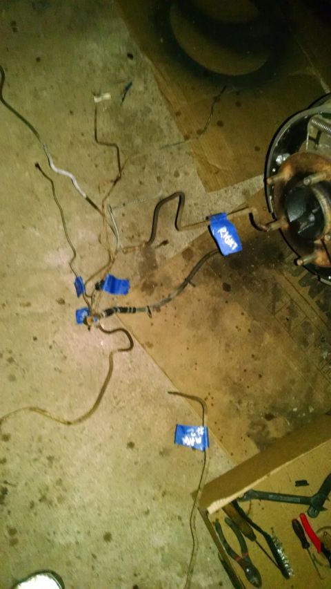 1994 Ford Bronco - A collection of brake lines and electrical wires are laid out on a concrete floor, with some marked with blue tape and writing. A portion o…