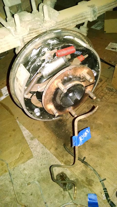 1994 Ford Bronco - A close-up view of the rear drum brake assembly of a vehicle, showing brake shoes, springs, and a wheel cylinder. A brake line is visible w…