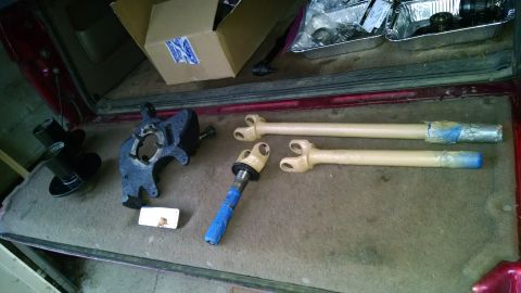 1994 Ford Bronco - Several automotive parts, including a painted steering knuckle, two driveshafts wrapped in plastic and tape, and two black hub assemblies,…