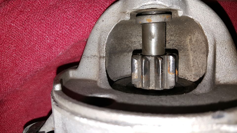 Close-up of a starter motor drive gear with rust, set against red fabric.