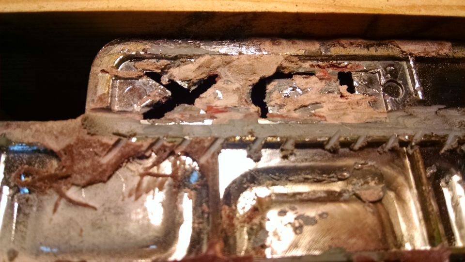 Close-up of heavily corroded and damaged chrome-plated vehicle part with rust and material loss.
