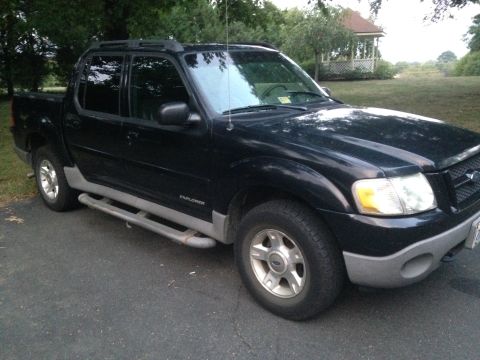 2001 Ford Explorer - A black 2001 Ford Explorer Sport Trac pickup truck is parked on an asphalt driveway in front of a grassy lawn with trees and a gazebo in th…