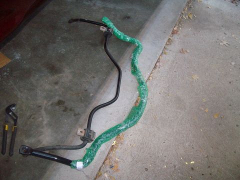 2004 Ford Crown Victoria - A black sway bar, partially wrapped in green plastic, lies on a concrete surface next to a pair of channel lock pliers.