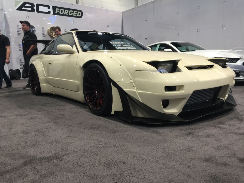 Cream custom Nissan 240SX coupe with widebody kit and dark red wheels.