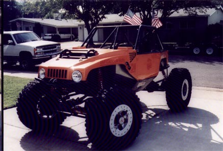 1990 Ford Bronco - This custom off-road buggy features oversized tires and American flags, parked in a driveway with another vehicle visible.