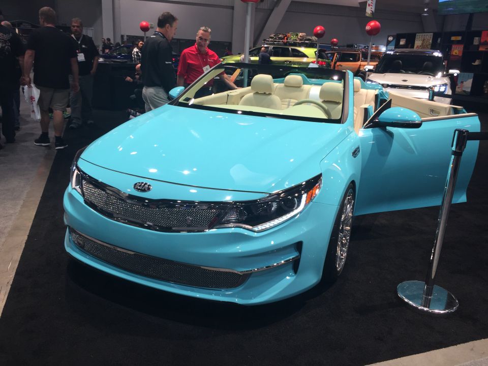 Turquoise convertible Kia Optima with cream interior at an auto show.