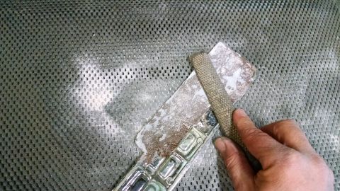1992 Ford Bronco - A hand uses a rasp to file a chrome car badge that has segmented rectangular details.