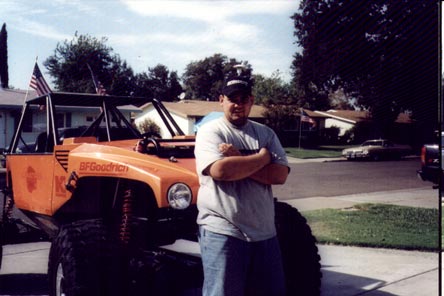 1990 Ford Bronco - Man poses with a heavily modified off-road vehicle in a residential area.