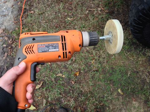 1979 Ford Bronco - A hand holds an orange drill with a polishing pad, positioned near a vehicle tire, suggesting detailing or repair work.
