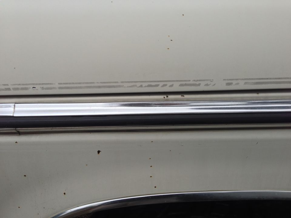 Close-up of light-colored car body with chrome trim and faint pinstripe detail. Watermark reads SUPERMOTORS