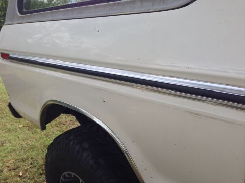 1979 Ford Bronco - Close-up of a white Ford Bronco's side panel, revealing chrome trim and a fender flare.