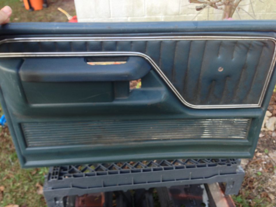Dark teal car door panel with vertical stitching and chrome trim, resting on a black crate