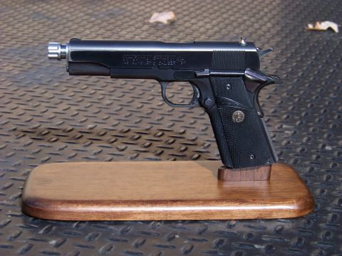 1995 Mercury Grand Marquis - A Colt 1911 pistol is shown on a wooden display stand against a textured background.