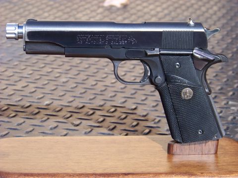 1995 Mercury Grand Marquis - A close-up side view of a black semi-automatic handgun with a threaded barrel and textured grip, resting on a wooden stand.