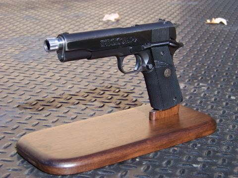1995 Mercury Grand Marquis - A black semi-automatic pistol is displayed on a wooden stand. The pistol is resting on a diamond plate surface.
