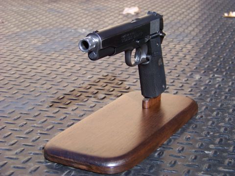 1995 Mercury Grand Marquis - A black semi-automatic handgun is displayed on a wooden stand against a textured metal background.