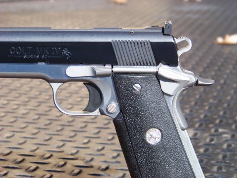 1995 Mercury Grand Marquis - A close-up, side profile view of a black and silver Colt MK IV Series 80 semi-automatic pistol. The firearm is resting on a textured, diamo…