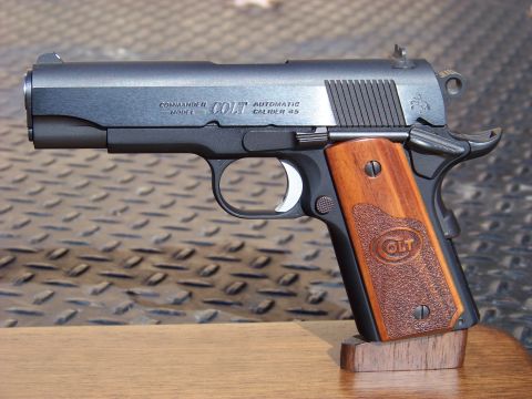 1995 Mercury Grand Marquis - A close-up, side view of a Colt Commander Model automatic caliber .45 pistol with wooden grips rests on a wooden stand.