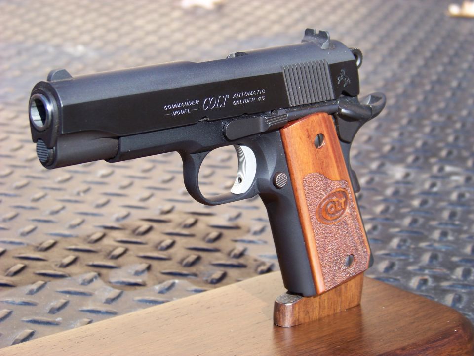 Colt Commander semi-automatic pistol with wooden grips on a wooden stand.
