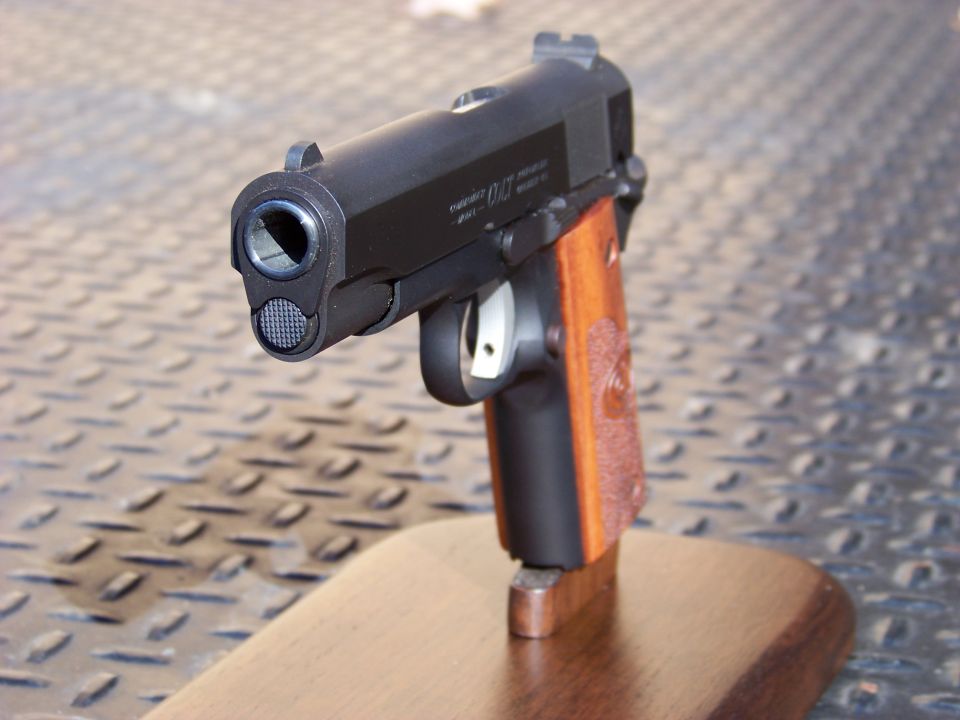 Black semi-automatic pistol with wooden grips on a wooden stand, front view.