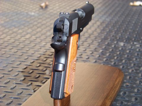 1995 Mercury Grand Marquis - A close-up, angled view of the rear of a black semi-automatic pistol with wooden grips, resting on a wooden stand. The pistol is shown agai…