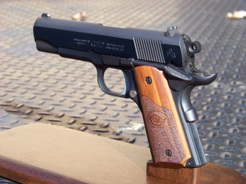 1995 Mercury Grand Marquis - A close-up, angled view of a black Colt Commander semi-automatic pistol with wooden grips.