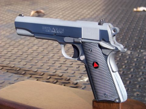 1995 Mercury Grand Marquis - A close-up, angled view of a silver and dark blue semi-automatic pistol with "DELTA ELITE" and "COLT .45 AUTO-" markings on the slide. The…