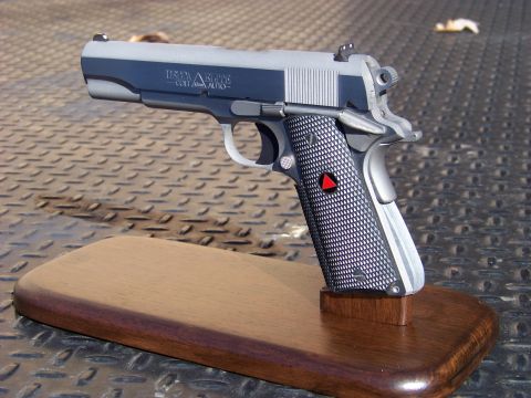 1995 Mercury Grand Marquis - A close-up, angled view of a pistol displayed on a wooden stand. The pistol is two-toned with a dark blue slide and a silver frame, featuri…