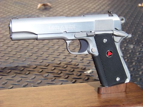 1995 Mercury Grand Marquis - A silver semi-automatic handgun with black grips is displayed on a wooden stand. The handgun has "DELTA ELITE" and "COLT 10mm AUTO" text vi…