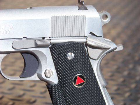 1995 Mercury Grand Marquis - A close-up, detailed view of the side of a silver semi-automatic handgun. The grip features black textured panels with a circular emblem co…