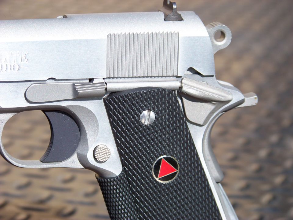 Close-up of a silver semi-automatic pistol grip with a red triangle emblem.