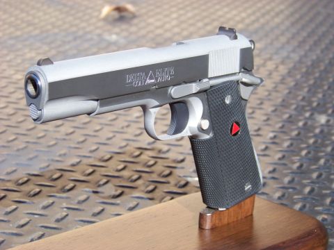 1995 Mercury Grand Marquis - A close-up, angled view of a Colt Delta Elite 10mm Auto pistol resting on a wooden stand. The pistol is silver and black with textured blac…