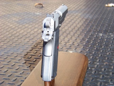 1995 Mercury Grand Marquis - A close-up, rear-facing view of the top of a silver handgun resting on a wooden block. The handgun is positioned on a textured metal surfac…