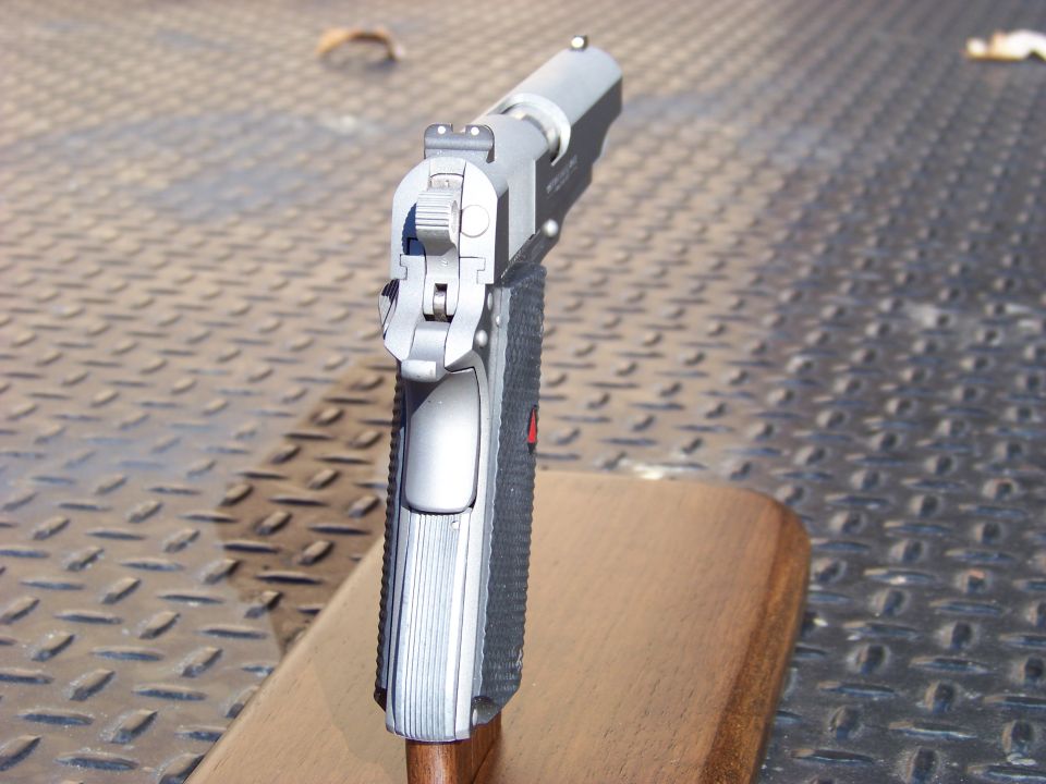 Rear view of a silver handgun on a wooden block and metal surface.