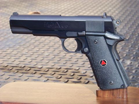 1995 Mercury Grand Marquis - A black semi-automatic pistol with a Delta Force logo on the grip is displayed on a wooden stand against a textured metal background.