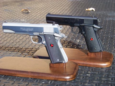 1995 Mercury Grand Marquis - Two handguns are displayed on wooden stands. The handgun in the foreground is silver and black with "DELTA ELITE COLT AUTO" written on the…