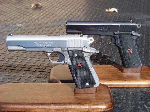 1995 Mercury Grand Marquis - Two handguns are displayed on wooden stands on a textured metal surface. The handgun in the foreground is silver with black grips and "DELT…