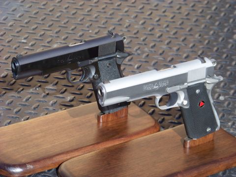 1995 Mercury Grand Marquis - Two handguns, a black Colt 1911 and a silver Colt Delta Elite, are displayed on wooden stands against a diamond plate background.