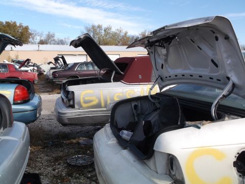 1999 Mercury Grand Marquis - Several cars are parked in a junkyard with their trunks open. One car has yellow spray paint on its trunk that reads "Gliss".