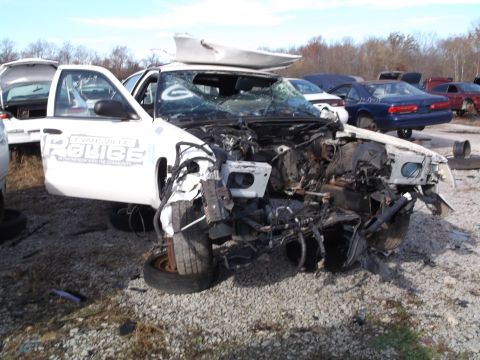 1999 Mercury Grand Marquis - A heavily damaged white police car is parked in a junkyard with its front end destroyed. The car has "EVANSVILLE POLICE" written on the sid…