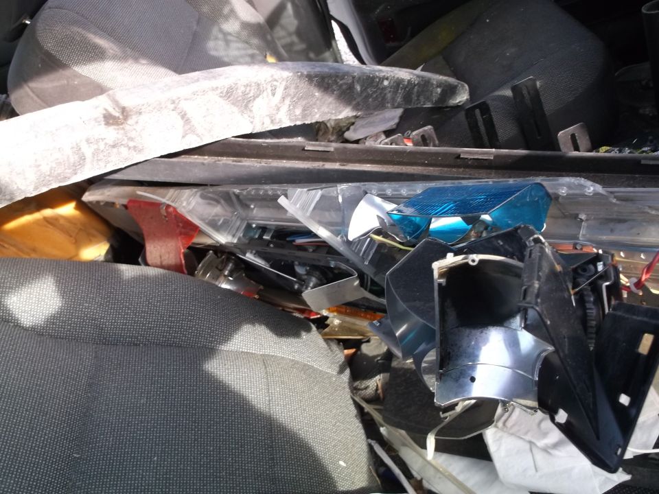 Pile of car parts inside a vehicle, including blue reflector and black housing.