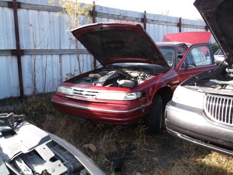 1999 Mercury Grand Marquis - A red sedan with its hood open is parked in a grassy lot next to a silver sedan with its hood also open. A white metal fence runs along the…