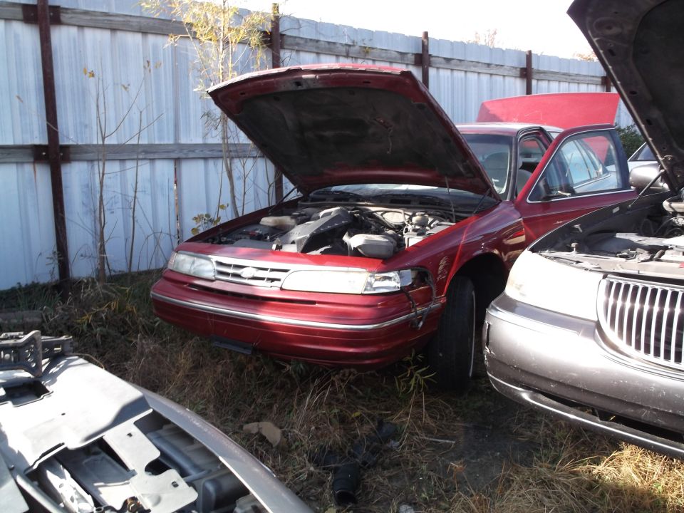 Red sedan with hood open in a junkyard setting.