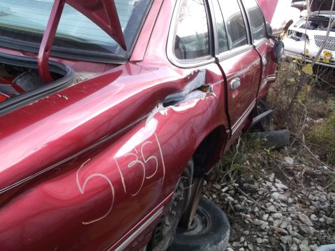 1999 Mercury Grand Marquis - The rear quarter panel of a damaged red sedan has white chalk markings that read "51351". The trunk is open, revealing the interior, and th…