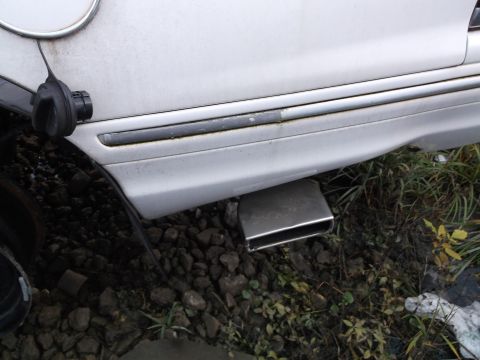 1999 Mercury Grand Marquis - A close-up view of the rear passenger side of a white sedan, showing the fuel filler door and a chrome exhaust tip protruding from the lowe…