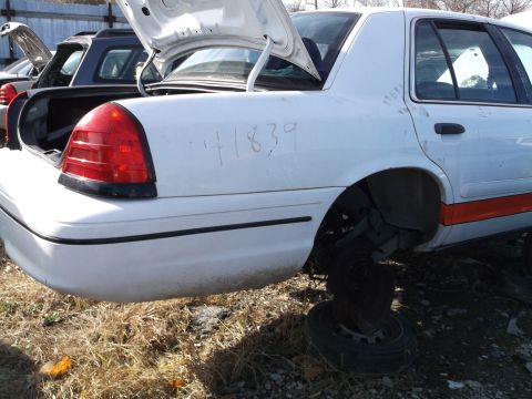 1999 Mercury Grand Marquis - The rear quarter panel of a white sedan shows the number "41839" written in marker. The car is missing its rear wheel and has an orange str…